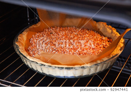 A glass baking dish with shortbread dough with dried peas, so that it does not rise, is baked in the oven A glass baking dish with shortbread dough with dried peas, so that it does not rise, is baked in the oven 92947441