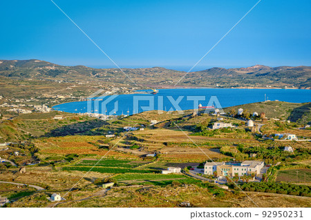 Beautiful view of Adamantas town, bay and villages of Milos island at sunset, Greece. Whitewashed houses, green hills, low sun, blue sea, clear sky, 92950231