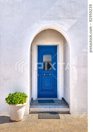 Traditional blue door and whitewashed walls of Greek house entrance and flower pot with rich foliage. Midday, summer sunshine, Milos, Greece 92950239