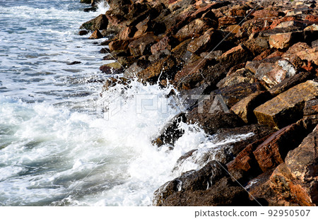Breakwater with waves in sea. Waves at the stone pier. A big wave in storm breaks on stones at pier  92950507