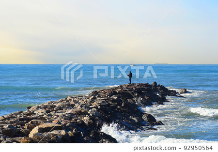 Fisherman on Masonry breakwater. A fisherman catches fish in the sea on a stone breakwater. Fisherman on Masonry breakwater. A fisherman catches fish in the sea on a stone breakwater. 92950564