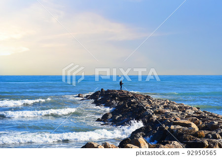 Fisherman on Masonry breakwater. A fisherman catches fish in the sea on a stone breakwater. Fisherman on Masonry breakwater. A fisherman catches fish in the sea on a stone breakwater. 92950565