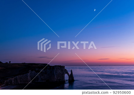 The crescent moon floating in the evening sky and the silhouette of the cliffs of the Etretat coast 92950600