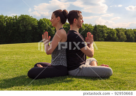 Young healthy man and woman doing yoga in the sunny summer park. Fitness and healthy lifestyle Young healthy man and woman doing yoga in the sunny summer park. Fitness and healthy lifestyle 92950668