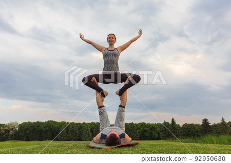 Young couple doing acro yoga in park. Man lying on grass and balancing woman in his feet Young couple doing acro yoga in park. Man lying on grass and balancing woman in his feet 92950680