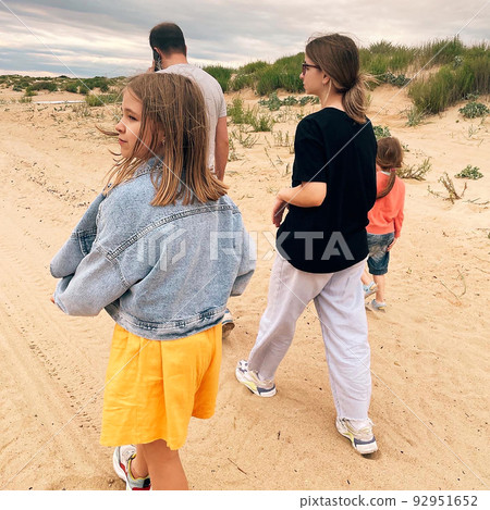 Rear view of family father and three daughters walking along wild sandy beach during adventure trip Rear view of family father and three daughters walking along wild sandy beach during adventure trip 92951652