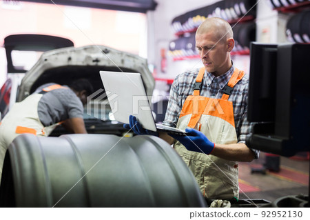 Mechanic with laptop near car engine in auto service Mechanic with laptop near car engine in auto service 92952130