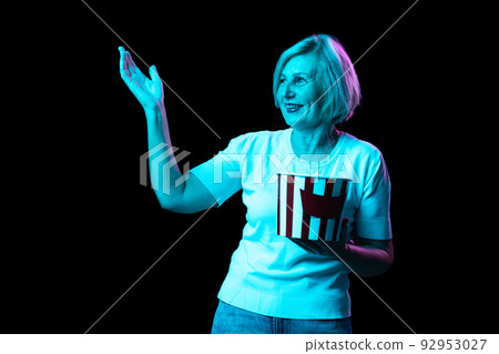 One excited senior woman, modern grandmother holding bucket of popcorn isolated on dark background in neon. Concept of emotions, facial expression, aspiration 92953027