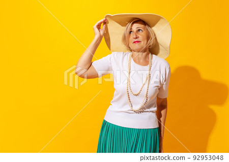 Sad mood. Elegant senior woman in summer style outfit and hat isolated on bright yellow background. Concept of beauty, emotions, vacation, travel Sad mood. Elegant senior woman in summer style outfit and hat isolated on bright yellow background. Concept of beauty, emotions, vacation, travel 92953048