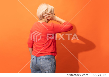 Back view of middle age woman with blond hair posing isolated on orange color background. Concept of emotions, facial expressions Back view of middle age woman with blond hair posing isolated on orange color background. Concept of emotions, facial expressions 92953103