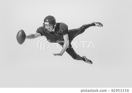 Dynamic portrait of young man, american football player catching ball. Black and white photography. Full equipment 92953158