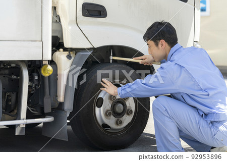 A man in work clothes checking the air pressure of truck tires Pre-operation inspection image 92953896