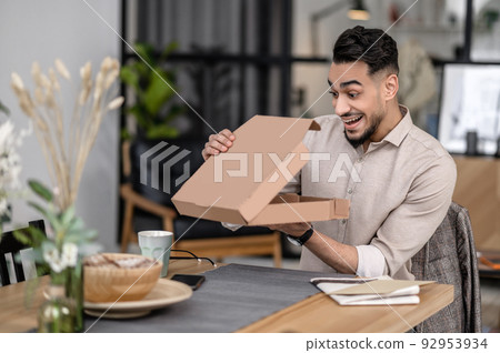 Man enthusiastically looking into open box sitting at table 92953934