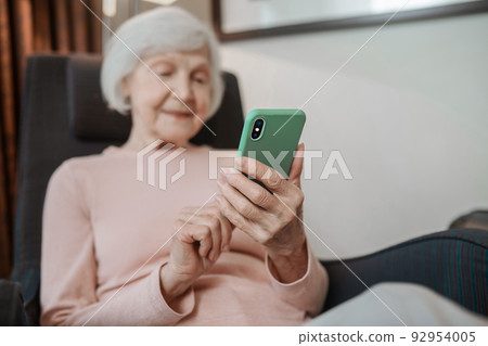Elderly lady in beige blouse with a smartphone in hand 92954005
