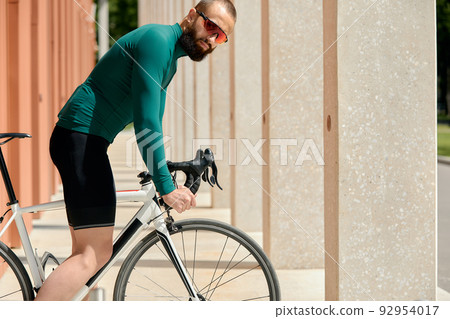 Caucasian handsome young man in protective helmet goes out for bicycle ride through city streets on blurred background. Cyclist male ride bike outdoors in urban. Caucasian handsome young man in protective helmet goes out for bicycle ride through city streets on blurred background. Cyclist male ride bike outdoors in urban. 92954017