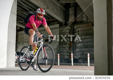 Portrait of a cyclist standing under a bridge with a bicycle, posing at the camera against an architecture background. Active lifestyle. Cycling is a hobby. Portrait of a cyclist standing under a bridge with a bicycle, posing at the camera against an architecture background. Active lifestyle. Cycling is a hobby. 92954056