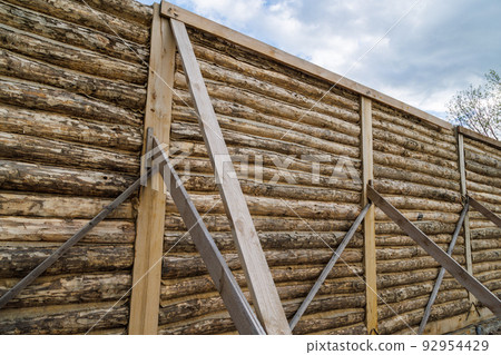 traditional wooden house peeled log wall during cobntruction process with diagonal props 92954429