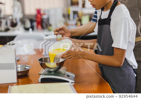 Boy helping mum pouring egg yolks into bowl for baking cake. Boy helping mum pouring egg yolks into bowl for baking cake. 92954644