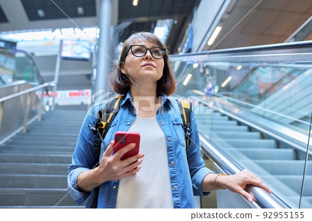 Middle-aged woman walking up stairs, near escalator in modern station buildin Middle-aged woman walking up stairs, near escalator in modern station buildin 92955155