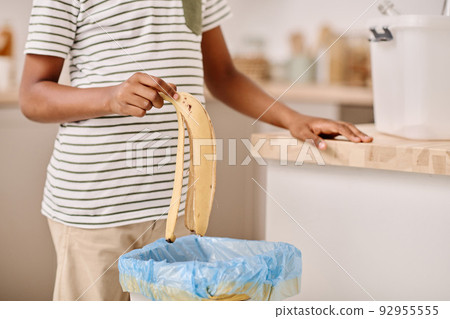 Close-up of African boy throwing banana peel into bucket while standing in the kitchen 92955555