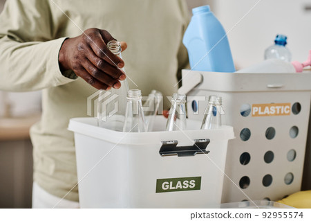 Close-up of African man separating glass bottles in container for recycling at home Close-up of African man separating glass bottles in container for recycling at home 92955574