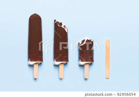 Chocolate covered ice cream on wooden stick consumption life cycle on blue background top view 92956054
