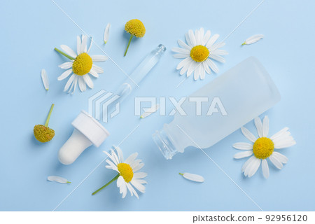Cosmetic skincare serum dropper and bottle with chamomile flowers and petals on blue  92956120