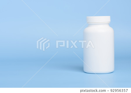 One white blank plastic medical pill or supplement bottle on blue background with copy-space One white blank plastic medical pill or supplement bottle on blue background with copy-space 92956357