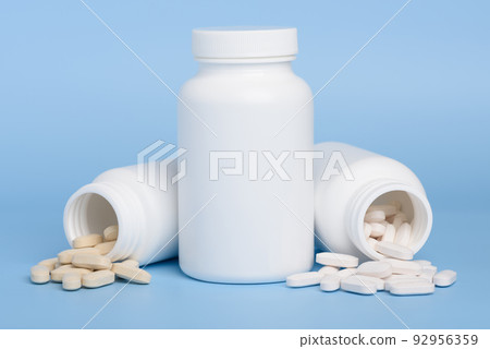 White medicine bottles, one closed and two with pills spilled on blue background with copy-space 92956359