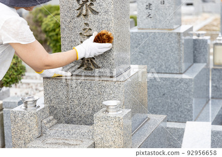 一個女人參觀墳墓並用刷子清潔它 一個女人參觀墳墓並用刷子清潔它 92956658