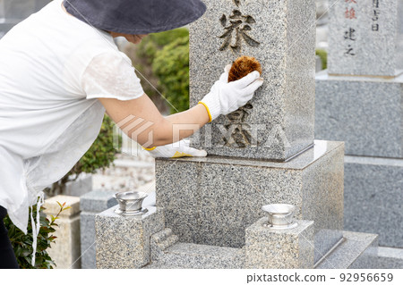 一個女人參觀墳墓並用刷子清潔它 一個女人參觀墳墓並用刷子清潔它 92956659