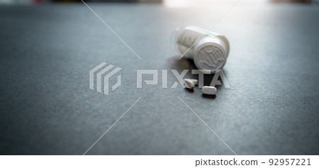 White tablets pills and blur child-resistant pill bottle on black table. Prescription drugs. Pharmaceutical industry. Medical care. Medication for cure illness. Pharmacy product. Small white tablets. 92957221