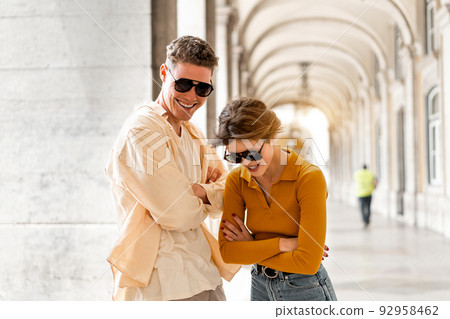 Young beautiful hipster couple in sunglasses in love walking on old city street Young beautiful hipster couple in sunglasses in love walking on old city street 92958462