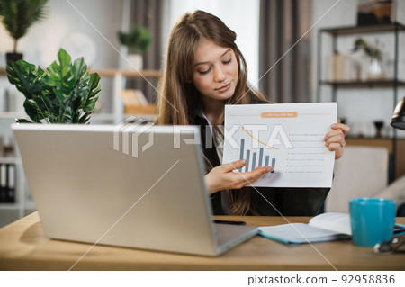Young woman freelance showing graphs and chart while sitting at table. 92958836