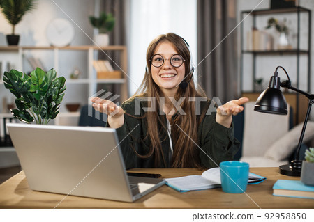 Young caucasian woman in headset sitting at desk with laptop and talking during video call. Young caucasian woman in headset sitting at desk with laptop and talking during video call. 92958850