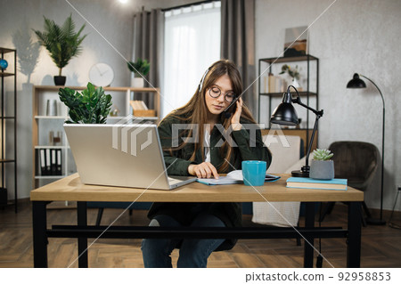 Young caucasian woman in headset sitting at desk with laptop and talking during video call. Young caucasian woman in headset sitting at desk with laptop and talking during video call. 92958853