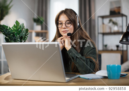 Young caucasian woman in headset talking during video chat on modern laptop. 92958858