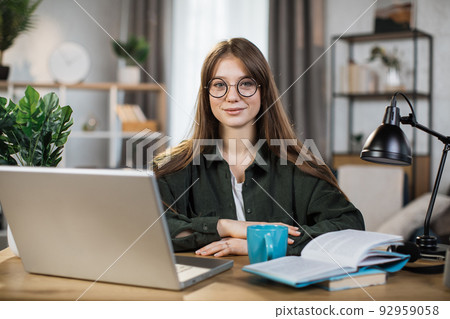 Pretty young caucasian woman with long dark hair sitting at table with modern laptop Pretty young caucasian woman with long dark hair sitting at table with modern laptop 92959058