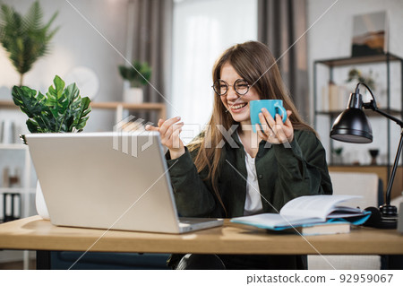 Excited young woman holding cup with hot drink and laptop for video conversation Excited young woman holding cup with hot drink and laptop for video conversation 92959067
