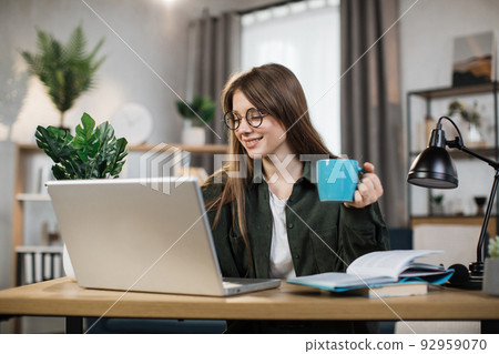 Attractive female freelancer with cup of coffee in casual outfit using modern laptop Attractive female freelancer with cup of coffee in casual outfit using modern laptop 92959070