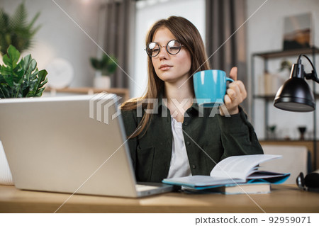 Attractive female freelancer with cup of coffee in casual outfit using modern laptop Attractive female freelancer with cup of coffee in casual outfit using modern laptop 92959071