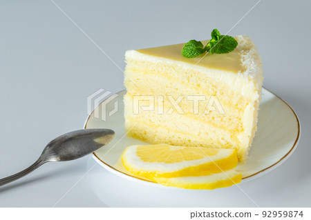 Piece of biscuit dessert with lemon and coconut flakes. Layered vanilla cake on white plate. Piece of biscuit dessert with lemon and coconut flakes. Layered vanilla cake on white plate. 92959874