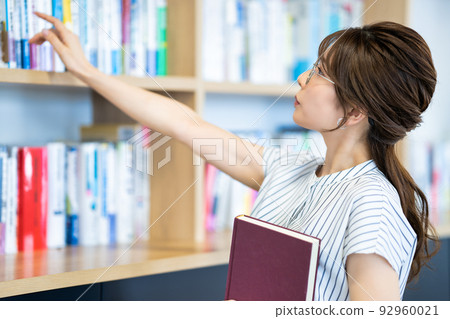 Young woman choosing a book from a bookshelf 92960021