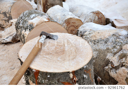 Axe on a chunk of firewood in the snow 92961762