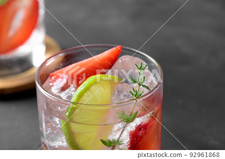 A glass with summer strawberry soda drink or mojito with strawberry, ice cubes and lime on dark background A glass with summer strawberry soda drink or mojito with strawberry, ice cubes and lime on dark background 92961868