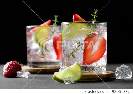 Two glasses with summer strawberry soda drink or mojito with strawberry, ice cubes and lime on dark background 92961872