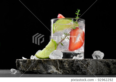 A glass with summer strawberry soda drink or mojito with strawberry, ice cubes and lime on dark background 92962292