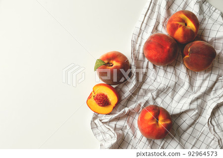 Ripe peaches whole and halved on white checkered fabric on white background 92964573