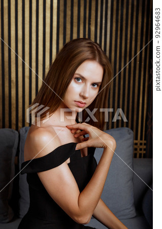 Young caucasian woman in evening dress sitting on couch at home looking at camera 92964683