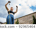 Attractive young fitness girl practising stretching exercise with rubber bands outdoors in the garden of her house. health and wellness concept. 92965464